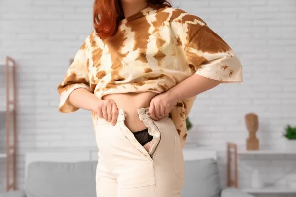 Image of woman trying to do her trousers up after pregnancy weight gain Sunbury
