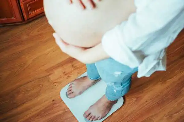 Image of woman weighing herself and experiencing weight gain through pregnancy Sunbury